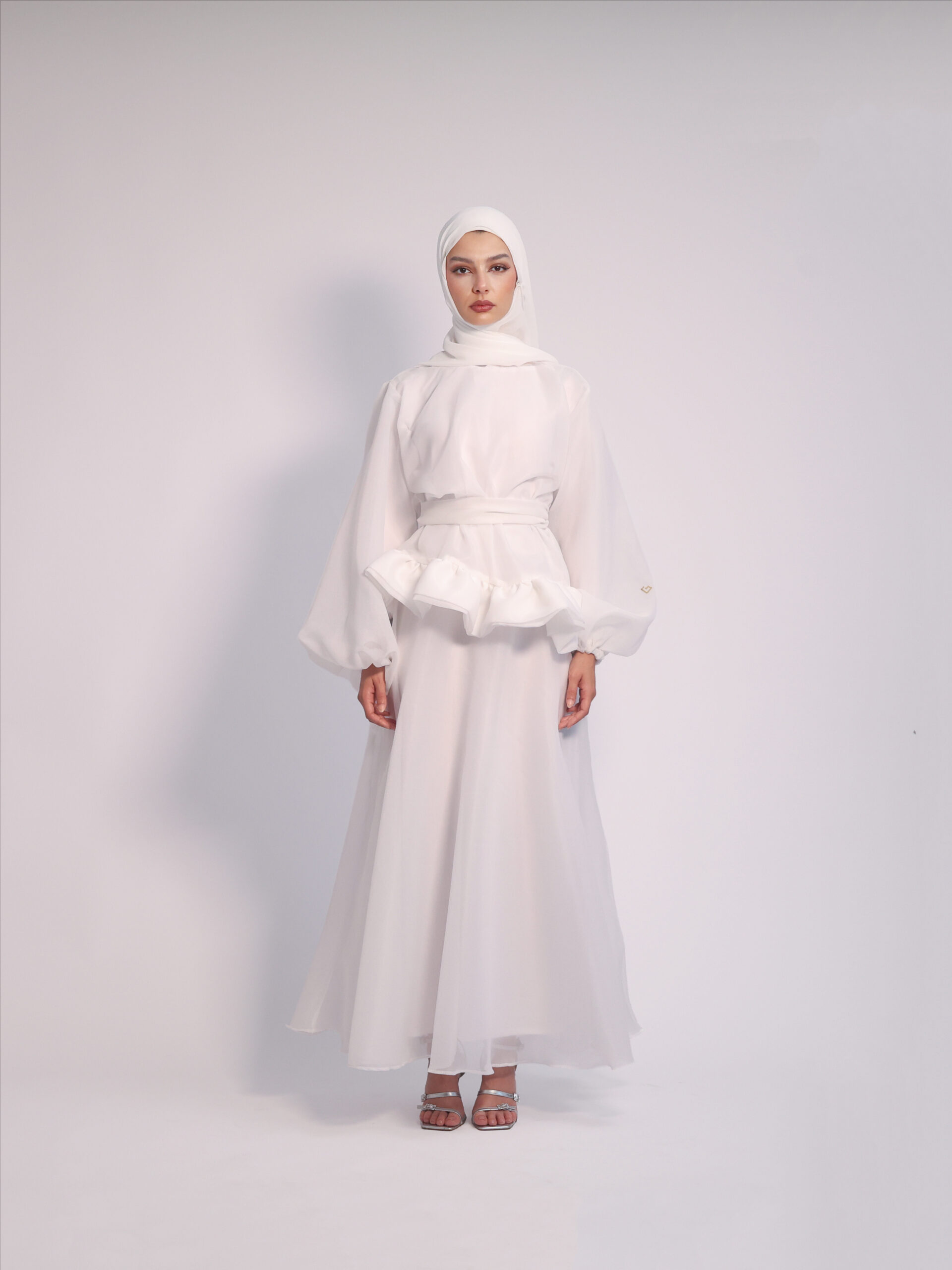 Cloud Peplum Dress in White by Kharzaat featuring a ruffled peplum waist, bishop sleeves, and flowing chiffon fabric
